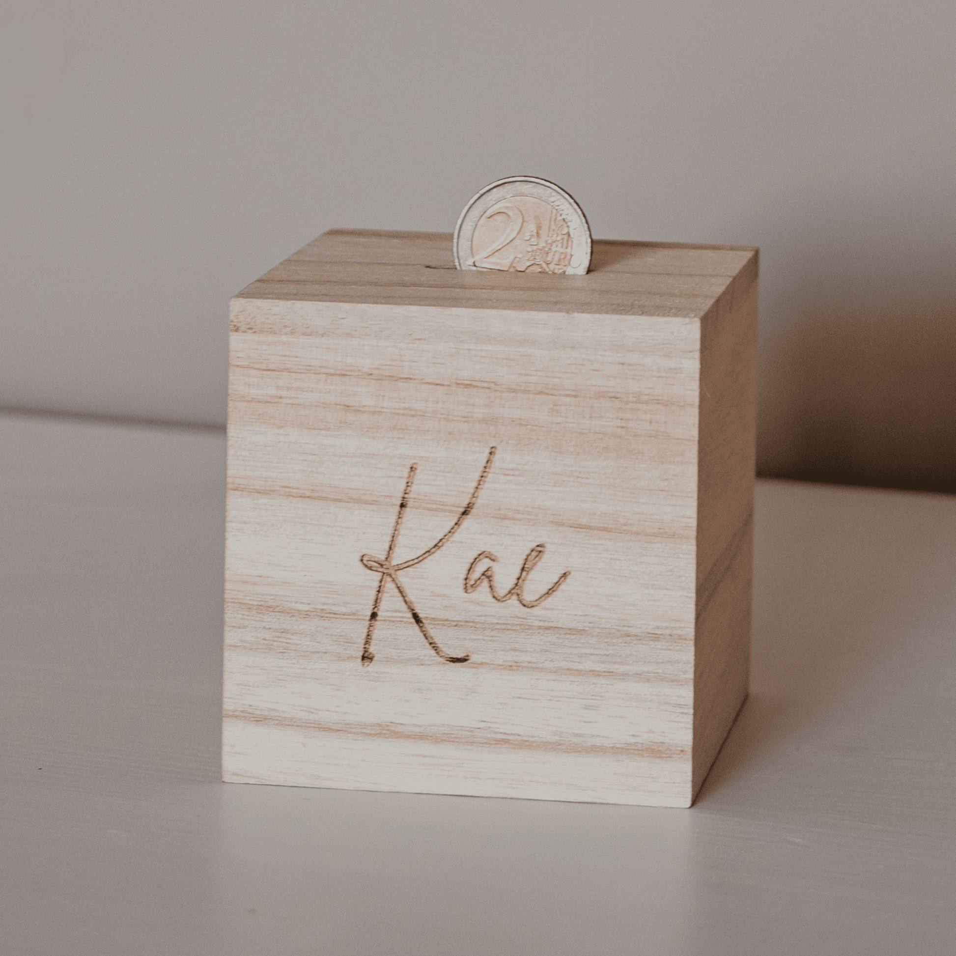 Houten spaarpot met naam –  foto in gebruik met 2 euro munt - een gepersonaliseerde spaarpot met gravure, ideaal als uniek cadeau. Deze houten spaarpot met naam is perfect voor kinderen om op een speelse manier te sparen.